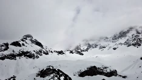 Timelapse-camera-left-to-right-panning-of-snowy-mountains-with-moving-fog,-clouds-and-snowfall