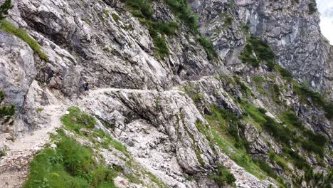 Panorámica-Lenta-De-Izquierda-A-Derecha-Que-Muestra-A-Un-Excursionista-Con-Casco-Naranja-Caminando-Por-Un-Sendero-Alemán-Alpino-Expuesto-Con-Clima-Nublado