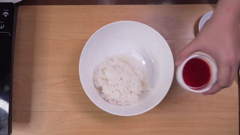 Placing-boiled-rice-into-white-bowl-and-mixing-it-with-red-sauce-and-oil