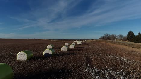 Sweeping-Drone-Aerial-shot-of-a-Midwestern-cotton-farm-with-fresh-bales-of-harvested-cotton-wrapped-in-bright-yellow-material-against-a-blue-open-sky