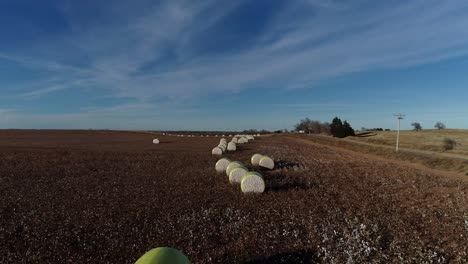 Slow-paced-sweeping-Drone-Aerial-shot-of-a-Midwestern-cotton-farm-with-fresh-bales-of-harvested-cotton-wrapped-in-bright-yellow-material-against-a-blue-open-sky