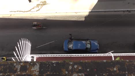 Typical-Cuban-city-street-with-vintage-cars,-motorcycles-and-people-passing-by,-birds-eye-view-from-rooftop-in-Matanzas
