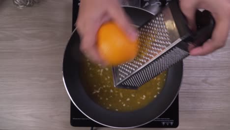 Close-up-on-female-hands-grating-orange-zest-into-frying-pan
