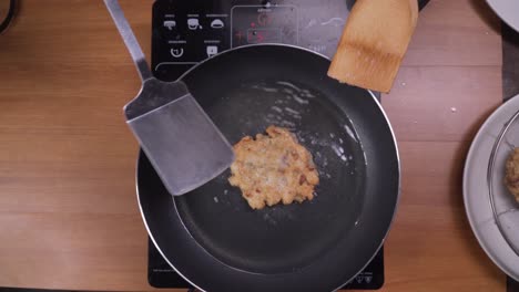 Cooks-hands-turning-over-small-fried-vegetable-pancake-with-spatula-and-ladle