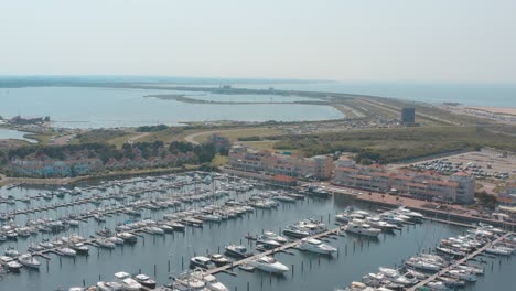 Cinematic-drone---aerial-tracking-panorama-shot-of-a-marina---port-with-sailing-boats-on-a-sunny-day-with-the-north-sea-in-the-background,-25p