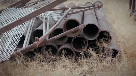 Rusty-abandoned-old-tubes-and-materials-stranded-in-the-middle-of-the-desert-with-dry-branches-being-slightly-moved-by-the-wind