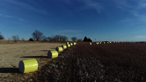 Sweeping-Drone-Aerial-shot-of-a-Midwestern-cotton-farm-with-fresh-bales-of-harvested-cotton-wrapped-in-bright-yellow-material-against-a-blue-open-sky