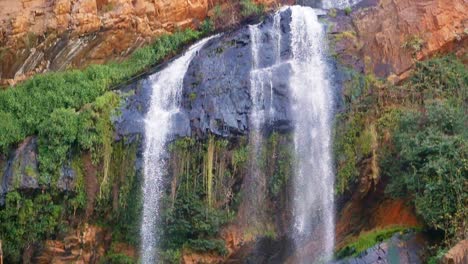Tilt-Down,-Slow-Motion-Waterfall-flowing-off-Rocky-Mountain-into-River-at-the-Walter-Sisulu-National-Botanical-Garden-in-Johannesburg,-South-Africa