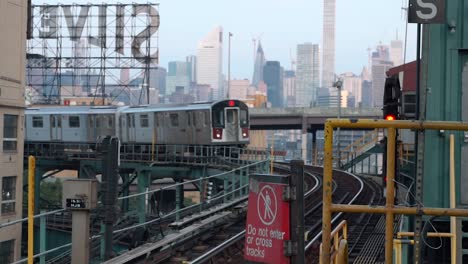 Incoming-seven-Train-at-Queensboro-Plaza-subway-station-with-the-Silvercup-Studios-and-the-Manhattan-skyline-in-the-background,-filmed-in-the-early-morning-hours-of-a-sunny-day-in-New-York-City