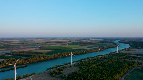 Luftkamerafahrt-Von-Oben-Auf-Fünf-Windkraftanlagen-In-Der-Nähe-Eines-Flusses-In-Südfrankreich-Bei-Sonnenuntergang
