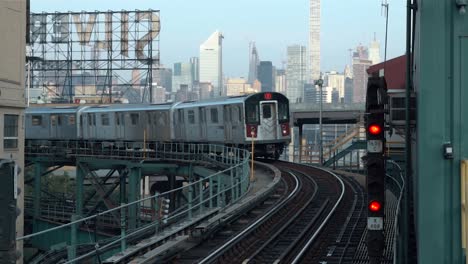 Incoming-train-at-the-Queensboro-Plaza-subway-station-with-the-skyline-of-Manhattan-and-the-Sivercup-Studios-in-the-background,-filmed-on-a-sunny-morning-in-New-York-City