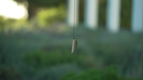 Close-up-shot-of-a-pendant-on-a-string-gently-moving-in-the-breeze-with-blurred-background