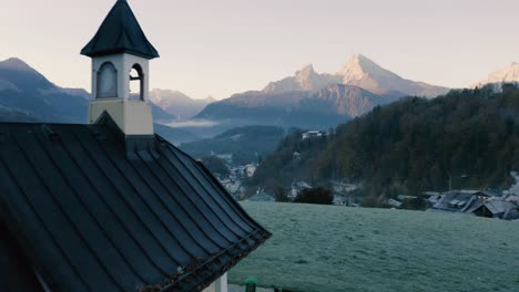 Autumn-Landscape-in-Bavaria,-Germany-|-4K-UHD-D-LOG---Cold,-misty-sunrise-Fall-colours-over-Berchtesgarden-Germany,-featuring-a-cinematic-drone-shot-of-a-chapel-overlooking-the-town---mountains