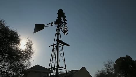 Handheld,-silhouette-of-windmill-spinning-on-the-backdrop-of-the-blue-sky-and-sunshine-on-a-windy-day