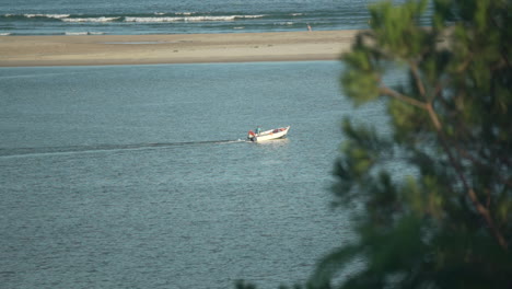 Still-shot-of-a-fishing-boat-motorboat-moving-across-the-water-with-a-tree-in-the-foreground