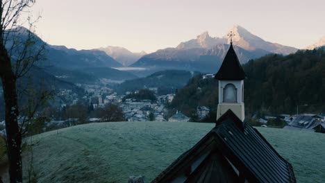 Autumn-Landscape-in-Bavaria,-Germany-|-4K-UHD-D-LOG---Cold,-misty-sunrise-Fall-colours-over-Berchtesgarden-Germany,-featuring-a-cinematic-drone-shot-of-a-chapel-overlooking-the-town---mountains