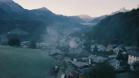 Autumn-Landscape-in-Bavaria,-Germany-|-4K-UHD-D-LOG---Misty-sunrise-Fall-colours-over-Berchtesgarden-Germany,-featuring-a-cinematic-drone-shot-flying-over-the-town---a-lumber-yard-with-steam