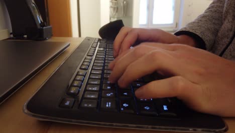 Caucasian-man-is-typing-on-a-black-LED-lit-keyboard-and-mouse