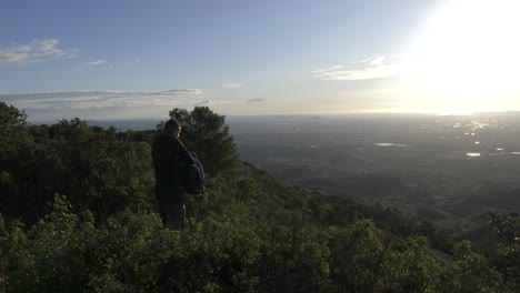 man-on-top-of-a-mountain-looking-for-sunglasses-in-his-rucksack-while-looking-at-the-sunrise