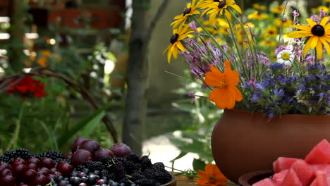 Basket-of-fresh-grapes-on-table-with-bouquet-of-autumnal-flowers-in-sunny-garden-pot
