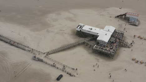 Drone---Aerial-top-shot-of-a-restaurant,-building-with-the-sandy-beach-with-tourists-and-people-in-St