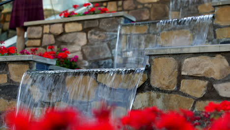 Defocus-view-of-red-poppy-flowers-with-waterfall-feature-on-stone-wall-in-the-background