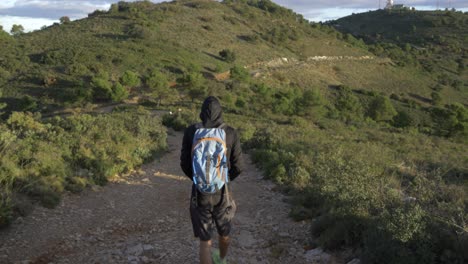 Man-on-top-of-a-mountain-hiking-down-the-mountain-at-sunrise-with-a-Black-hoodie-and-shorts