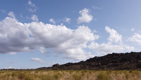 Wolken-Bewegen-Sich-Im-Zeitraffer-über-Eine-Teeplantage-Mit-Rotem-Busch-Und-Einem-Felsigen-Hügel-Im-Hintergrund