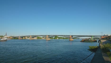 Panorama-shot-of-the-Theodor-Heuss-Brücke-bridge-between-the-cities-mainz-and-wiesbaden,-Hesse-and-rhineland-palatinate-with-the-river-rhine-and-a-cargo-ship-on-a-sunny-summer-day