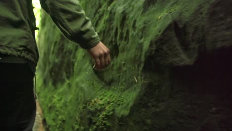 Hand-of-a-man-touches-and-slides-over-stones-with-green-moss-in-a-canyon-in-nature-close-up-tracking-shot