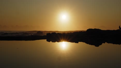 Slow-motion-shot-of-golden-sunrise-over-ocean-reflected-in-mirror-like-rock-pool