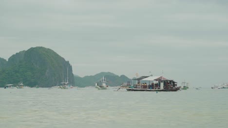 Eine-Gruppe-Von-Menschen,-Die-Eine-Bootsfahrt-Auf-Einem-Traditionellen-Hölzernen-Touristenboot-In-El-Nido,-Philippinen,-Genießen,-Mit-Bergen-Im-Hintergrund---Weitwinkelaufnahme
