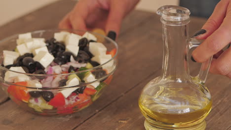 Olive-oil-being-poured-from-bottle-over-feta-salad-bowl-on-kitchen-table