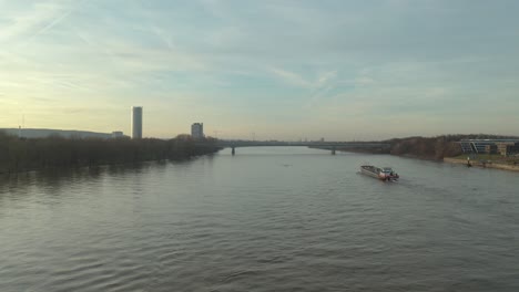 Cinematic-drone---aerial-shot-of-a-ship-on-the-river-rhine-in-bonn-with-the-post-tower-the-Kameha-Grand-Hotel-and-the-konrad-adenauer-bridge-at-the-golden-hour,-30p