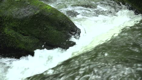 Fresh-flowing-water-brook-with-water-drops-in-the-nature-with-a-stone-with-moss-in-the-background-slow-motion-close-up-shot