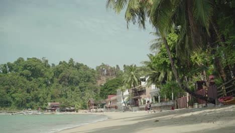 Tourist-Walking-Along-The-Tropical-Beach-in-El-Nido,-Philippines-Which-Composed-of-ExoticTrees-and-White-Sand-During-Sunny-Day---Perfect-For-Summer-Vacation---Wide-Shot