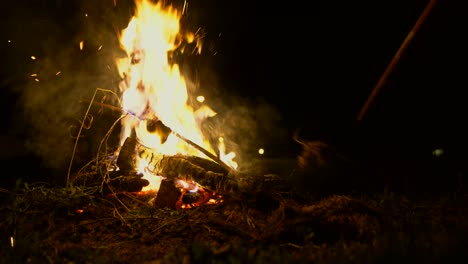 Static-shot-of-a-camp-fire-at-night-as-someone-adds-a-fresh-kindling-to-the-fire-and-rakes-the-logs-together