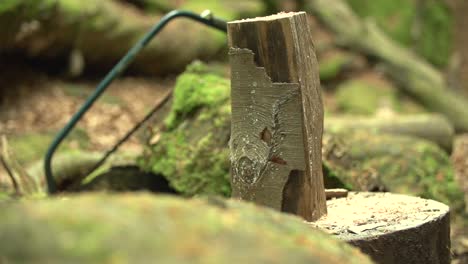 Slow-motion-close-up-shot-of-a-axt---hatchet-cutting---smashing-a-log-of-wood---billet-of-wood-with-a-saw-in-the-background