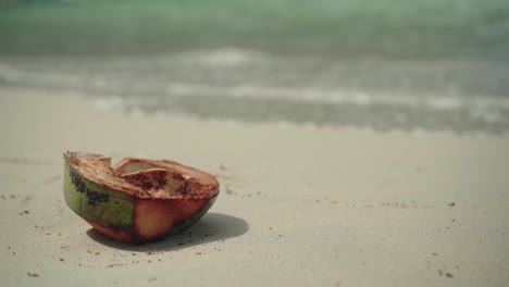 Coconut-Husk-On-The-White-Sand-With-Waves-Splashing-to-the-Tropical-Beach-in-El-Nido,-Philippines---Close-Up-Shot