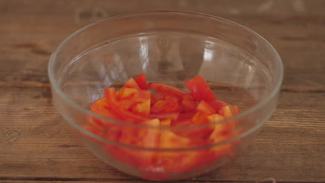 Fresh-sliced-tomato-pieces-being-placed-into-bowl-on-wooden-kitchen-table