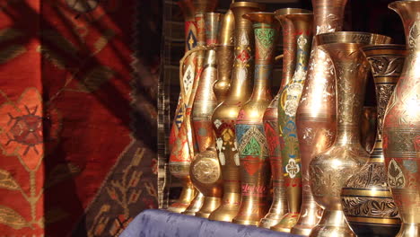 Selection-of-ornate-gold-plated-vases-lined-up-in-a-row-in-market-next-to-handmade-rug-in-Yerevan,-Armenia