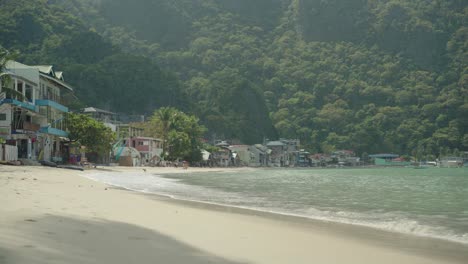 The-beautiful,-bright,-peaceful-beach-of-El-Nido,-Philippines-with-resort-rooms-facing-the-water-and-mountains-in-the-background---Wide-shot