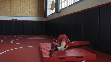 Teenage-wrestler-wearing-a-red-singlet-practicing-throws-on-a-dummy