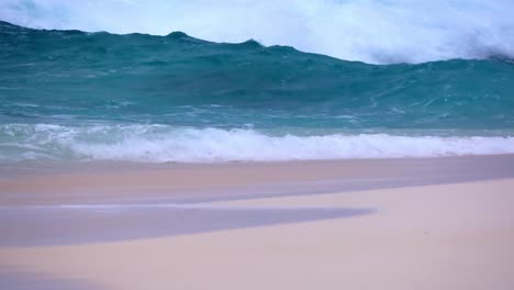 Blue-Waves-crashing-on-sandy-beach-on-small-island-in-tropics