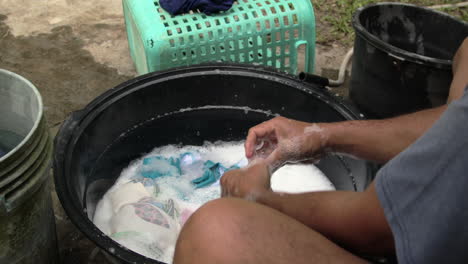 Man's-Hand-Washing-Dirty-Clothes-With-Bubbles-In-Black-Basin