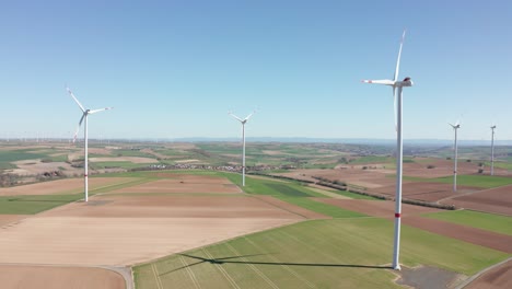 Rotating-wind-power-plant-producing-renewable-green-clean-engergy-electricity-in-a-wind-farm-on-a-sunny-day,-drone-aerial-rotating-panorama-shot,-25p