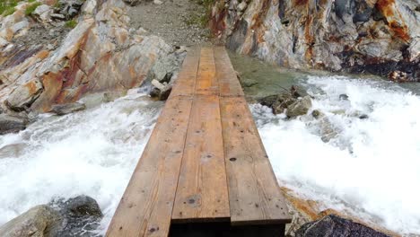 Sicht-Der-Hölzernen-Fußgängerbrücke-Ohne-Seile,-Die-über-Einen-Schnell-Fließenden-Alpenfluss-Führt