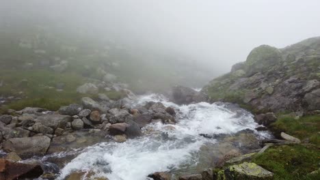 Static-view-of-fast-flowing-alpine-creek-flowing-on-a-rainy-foggy-day-in-rough-mountain-terrain