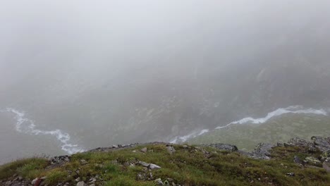 Right-to-left-aerial-pan-of-alpine-creeks-flowing-trough-the-mountains-on-a-rainy-and-foggy-day