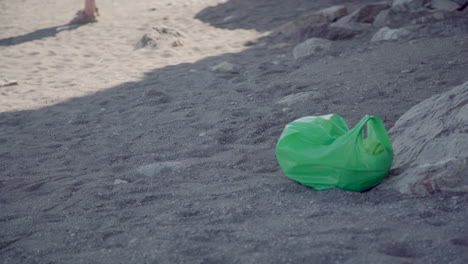 Green-plastic-bag-left-as-litter-at-beach,-human-impact-pollution